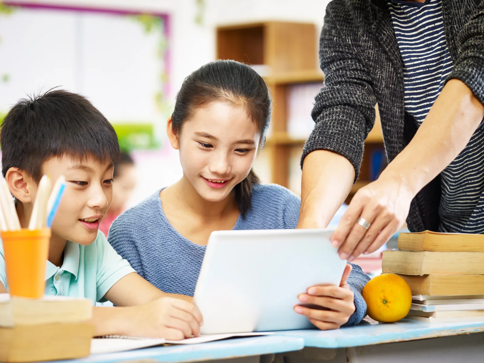 Two students looking at a tablet while a teacher points to the screen